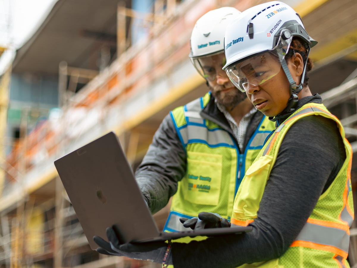 Two people working on a laptop at a construction site